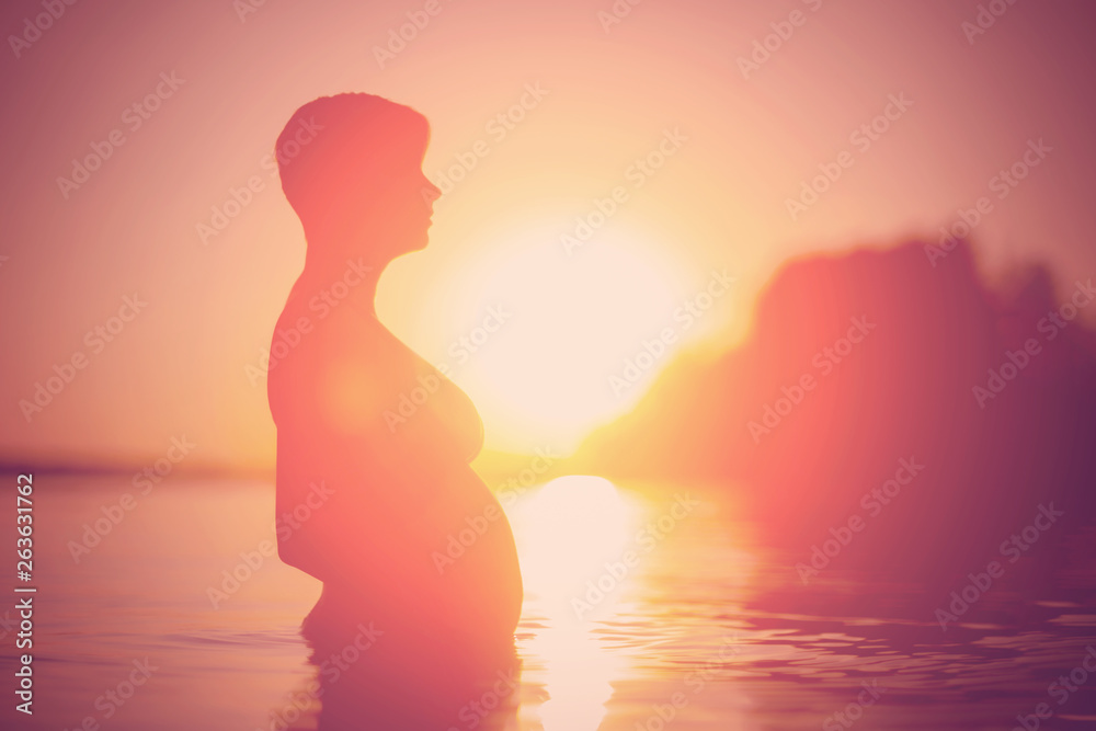 Silhouette of a pregnant woman in the water during sunset