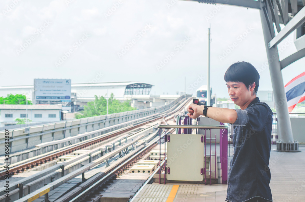 View of asian man stand and looking at his watch while waiting for something or worrying about time. Motion train as background. Business and travel concept. View of asian man stand and looking at his watch while waiting for something or worrying about time. Motion train as background. Business and travel concept.