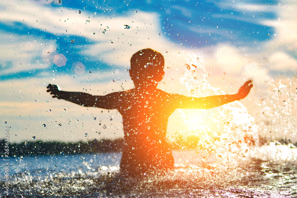 Silhouette of a child splashing in the water. Summer holiday.