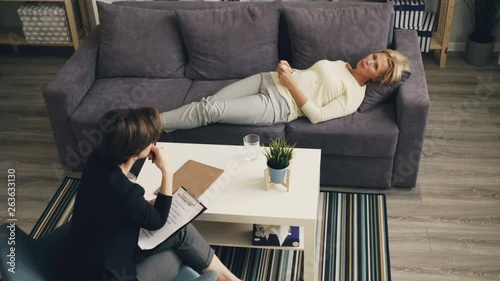 High angle view of mature lady sharing problems with female therapist lying on couch in office talking holding paper tissue. Conversation and psychology concept. photo