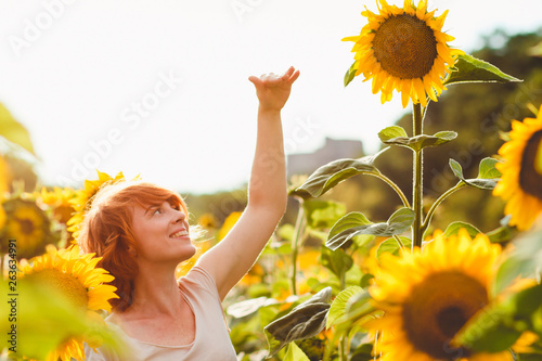 red-haired girl is standing next to a tall sunflower, a woman measures the height of a sunflower, her hand is lifted up