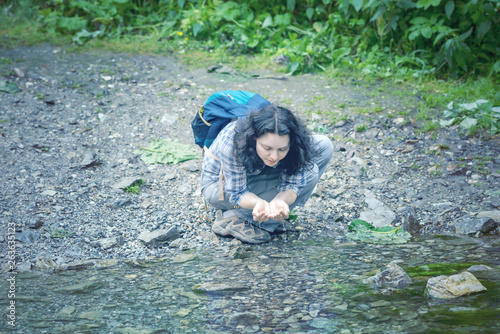 Fototapeta Naklejka Na Ścianę i Meble -  Tourist woman drinking water from a creek