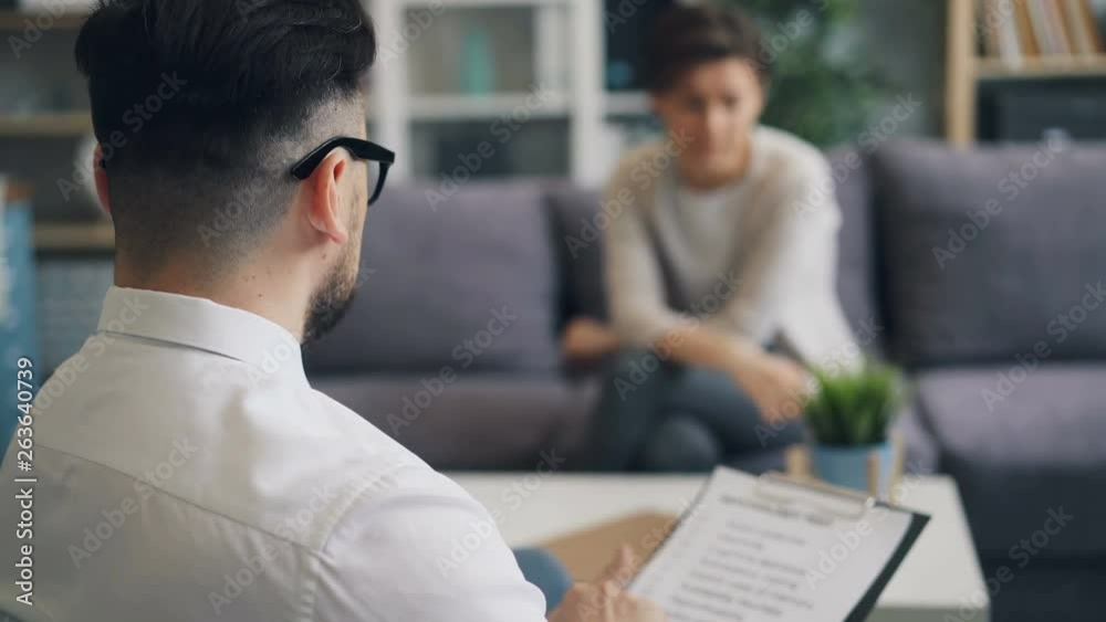 Successful psychologist bearded brunet is talking to female patient in office sitting holding paper asking questions. Profession, people and psychology concept.