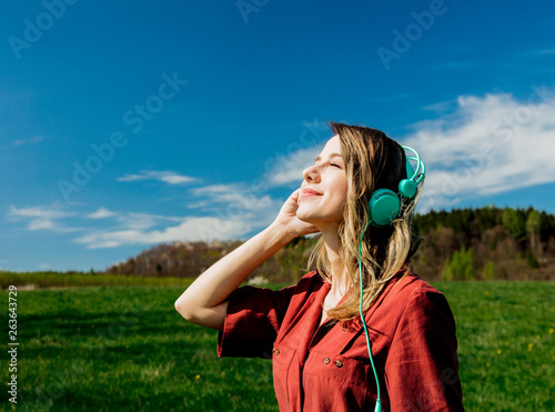 girl in red dress and hat have a carefree time with headphones on meadow