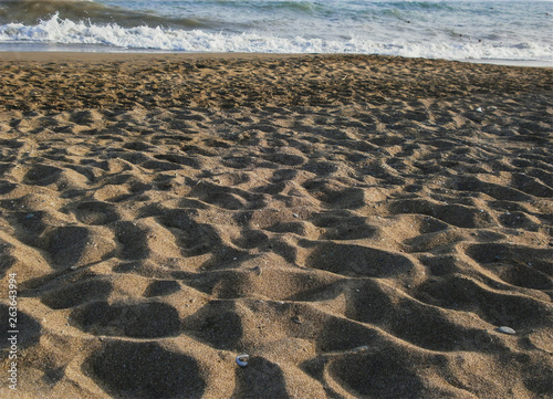 A beach of yellow sand  ashore sea wave runs up. On the sand there are grooves from the feet of tourists.