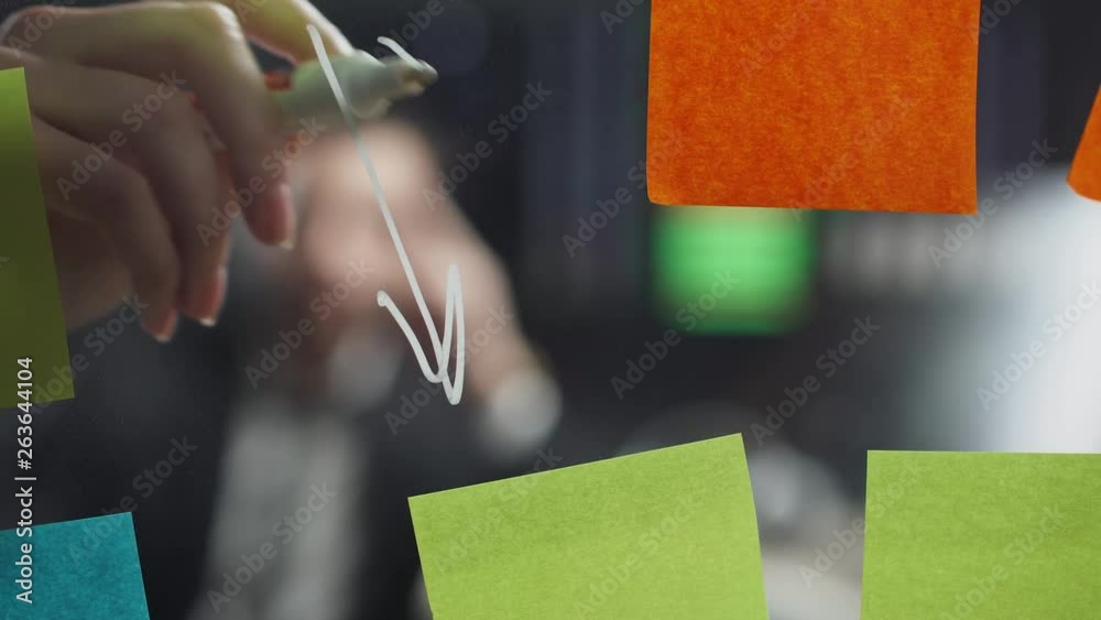 teamwork in modern office, man manager look at the board with sticky notes, women draws arrows infographic on the glass.