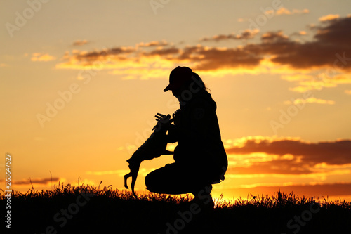 Silhouettes girl playing with a dog on the background of sunset, miniature pinscher breed, incredible sunset, best friends together