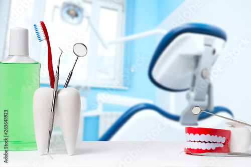Dental health and teethcare concept. Dental mirror with explorer probe and toothbrush in white tooth model near mouthwash. Human jaw model with dental floss against dental office and chair background