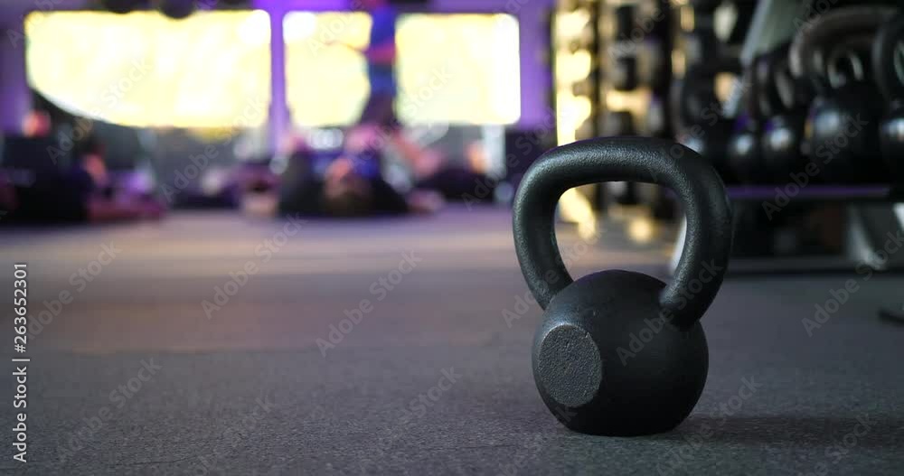 A kettlebell weight in a gym with people working out in a fitness training class in the background SLIDE RIGHT. A kettlebell weight in a gym with people working out in a fitness training class in the background SLIDE RIGHT.