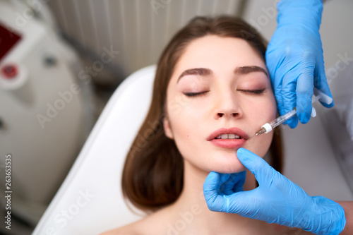 Lip Augmentation. Closeup Of Beautician Doctor Hands Doing Beauty Procedure To Female Lips with Syringe. Young Woman's Mouth Receiving Hyaluronic Acid Injection. Cosmetology Treatment. Filler Therapy.