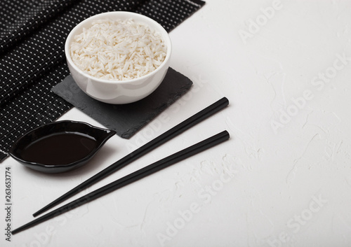 White bowl with boiled organic basmati jasmine rice with black chopsticks and sweet soy sauce on bamboo place mat on white background. Space for text