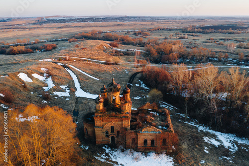 Aerial panoramic view of old abandoned russian orthodox church among beautiful countryside landscape in the spring with fields, trees and snow patches at sunset. Belogorka, Penza oblast, Russia photo