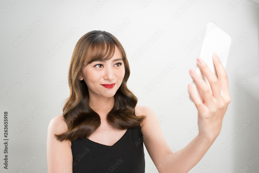 Smiling young girl making selfie photo on smartphone over gray background