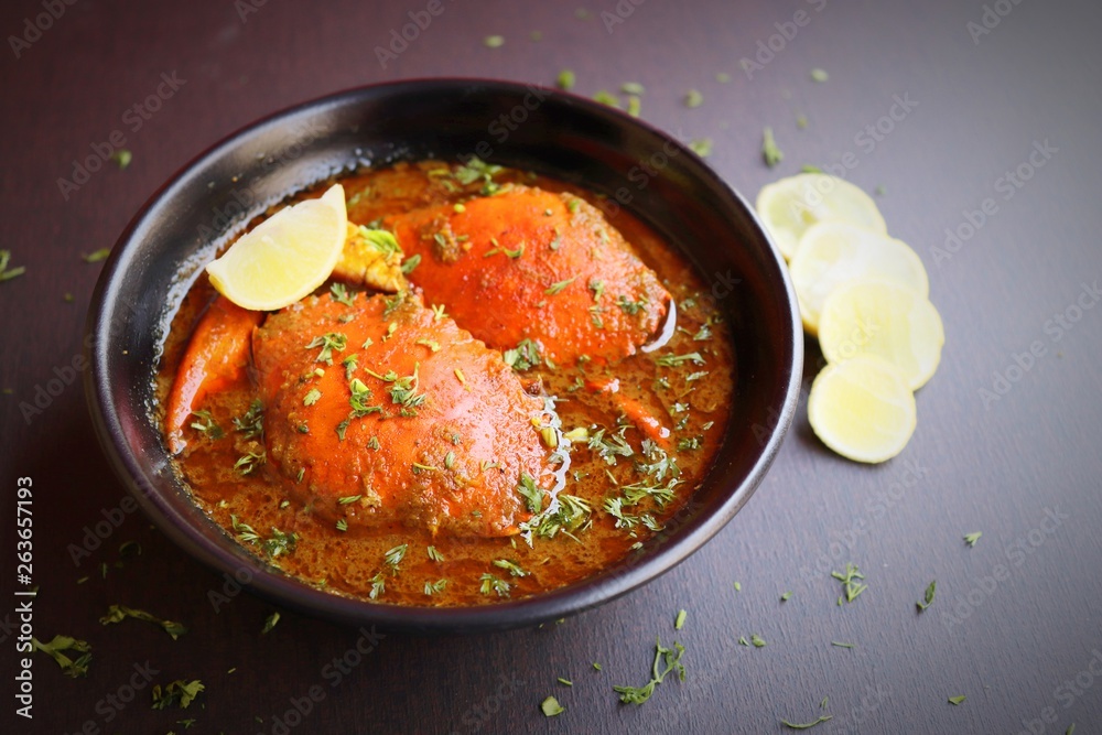 Indian Cuisine, Spicy Crabs Curry in red gravy, garnished with fresh coriander and lemon wedges or lemon slices on dark moody background Indian Cuisine, Spicy Crabs Curry in red gravy, garnished with fresh coriander and lemon wedges or lemon slices on dark moody background