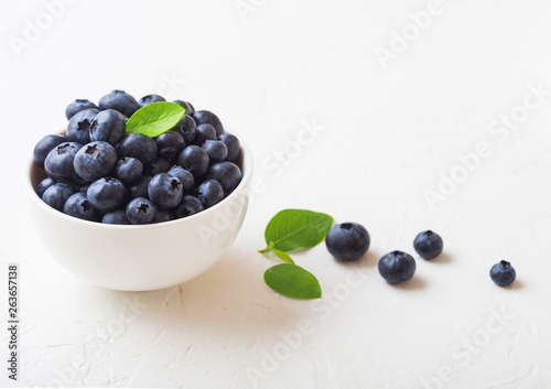 Fresh raw organic blueberries with leaf in white china bowl on white background. Macro close up