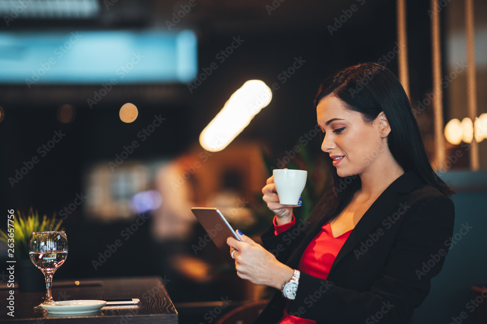 Young woman using digital tablet in a cafe with and holding a cup of coffee in hand