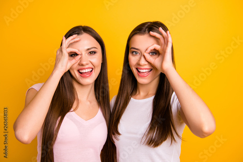Close up photo two people beautiful funky funny she her ladies models show okey symbol near eyes advising buy buyer novelty tested quality wear white pink casual t-shirts isolated yellow background