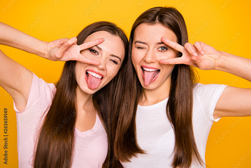 Close up photo of cute funny pretty girls trendy students best have free time travel make v-signs near eyes tongue-out feel satisfied careless isolated wear light-colored t-shirts yellow background Close up photo of cute funny pretty girls trendy students best have free time travel make v-signs near eyes tongue-out feel satisfied careless isolated wear light-colored t-shirts yellow background