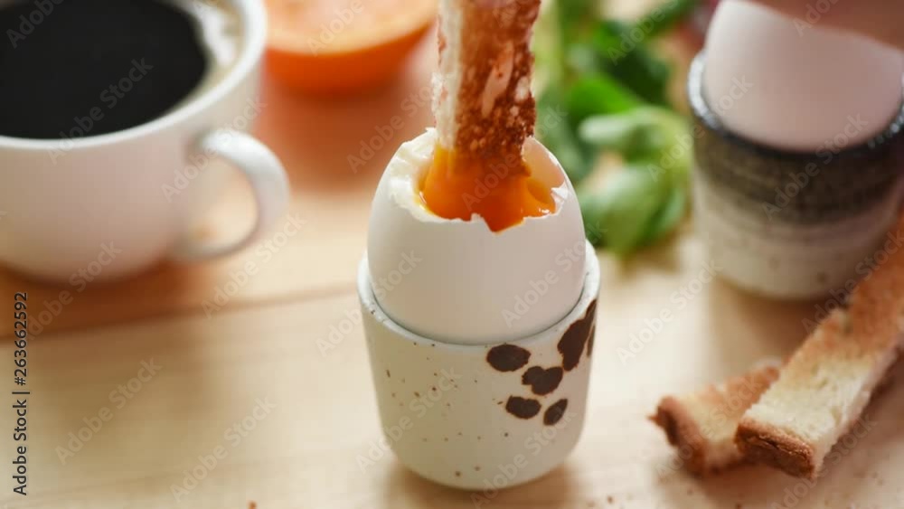 Dipping toasted bread into egg yolk in slow motion. Eating soft boiled egg. Tasty breakfast, closeup view