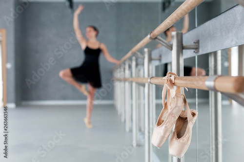 Pointe shoes hang on ballet barre. Blurred background with dancing ballerina. Girl has workout in ballet classic school.