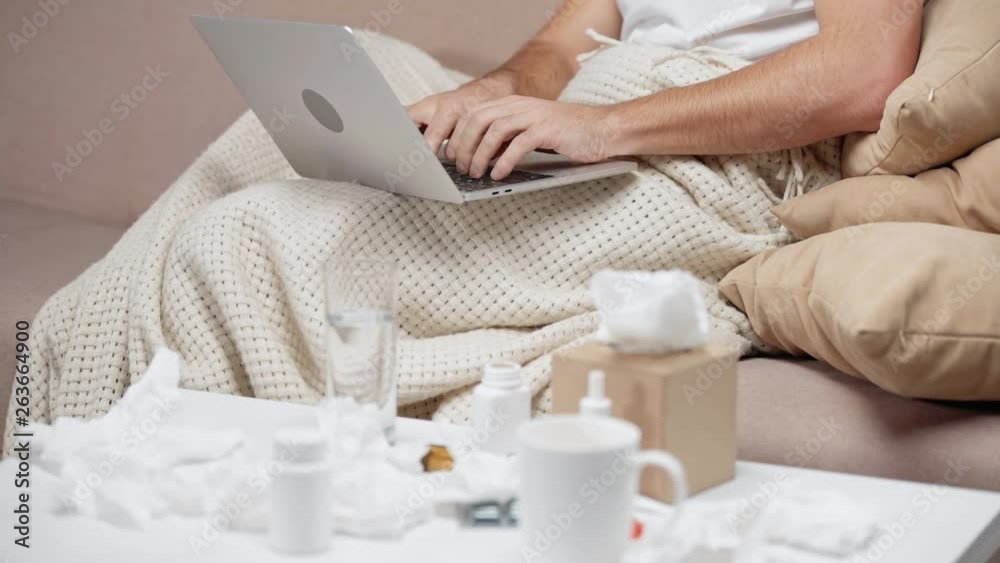 cropped view of sick blogger typing on laptop and taking tissue from tissue box on coffee table 