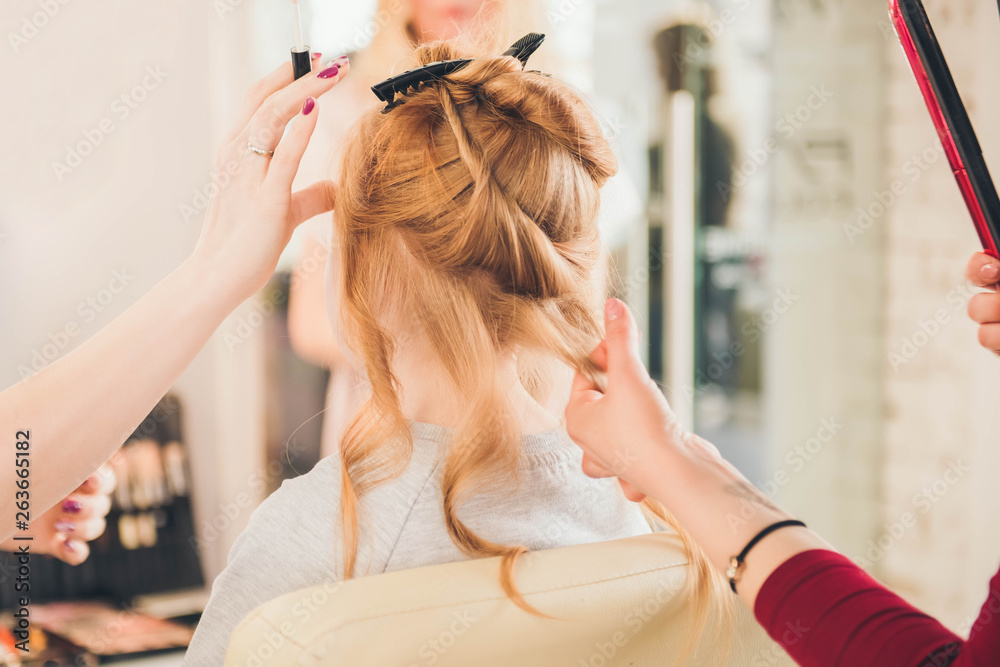 Fototapeta premium Сreating hairstyle. Children's hairdressing salon. Hairdresser curling hair for little girl. Make up.