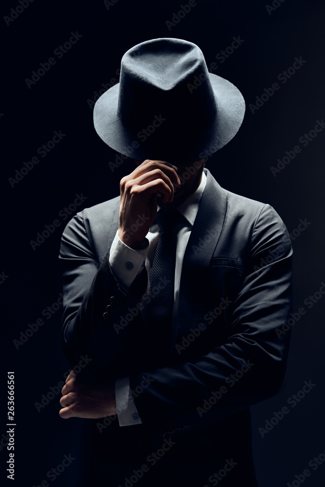 Man in suit hiding face behind his hat isolated on dark background Stock  Photo