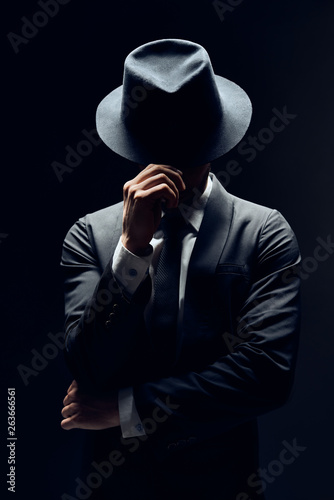 Man in suit hiding face behind his hat isolated on dark background photo