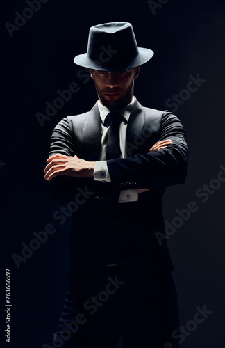 Foto Handsome confident man in black suit and hat with arms crossed on dark backgroun