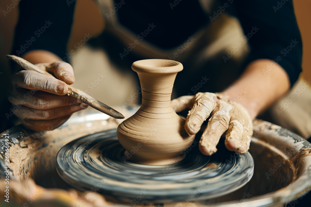 Man potter working on potters wheel making ceramic pot from clay in pottery workshop