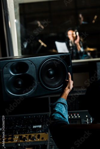 selective focus of mixed race sound producer showing thumb up to woman singing in recording studio