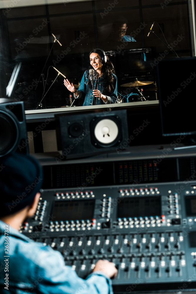 selective focus of mixed race sound producer working at mixing console while pretty woman singing in recording studio selective focus of mixed race sound producer working at mixing console while pretty woman singing in recording studio