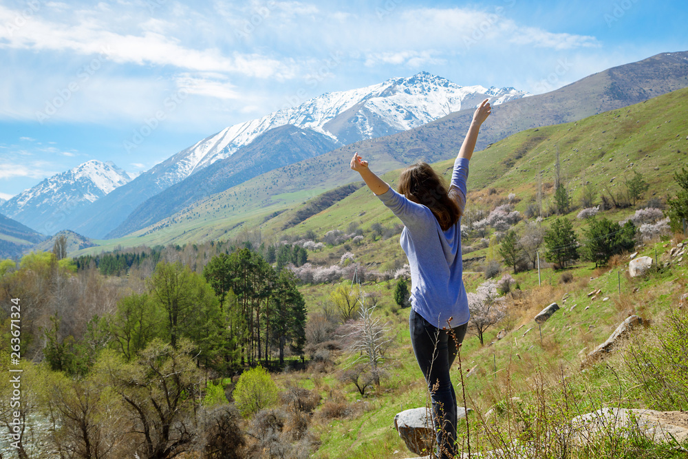 Young girl traveler on the background of spring mountains with their hands up. Nature and adventure. Young girl traveler on the background of spring mountains with their hands up. Nature and adventure.