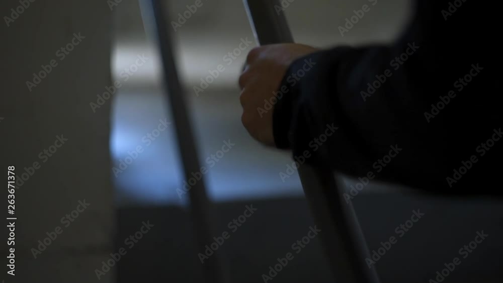 Closeup of Hand of a Man in Black Business Clothes Grasping Dark Stairwell Railing