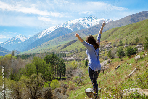 Young girl traveler on the background of spring mountains with their hands up. Nature and adventure. © Alwih