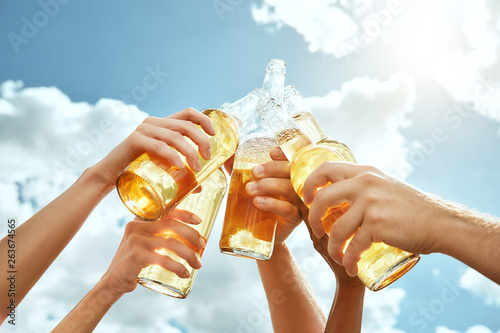 Beer time! Cropped image of hands are clinking bottles with beer against summer sky background. Barbecue concept.