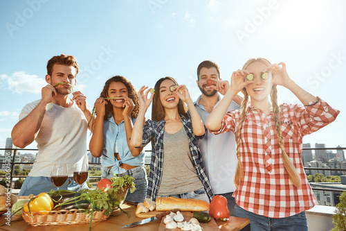 Enjoying time with friends. Group of young and cheerful friends in casual clothes preparing food for barbeque party and having fun while standing on the roof