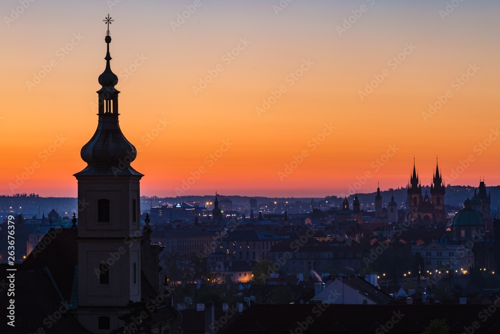 Prague, capital city of the Czech Republic, at dawn, horizon with pink, red, yellow, blue and orange sky, church tower in foreground, urban landscape, copy space