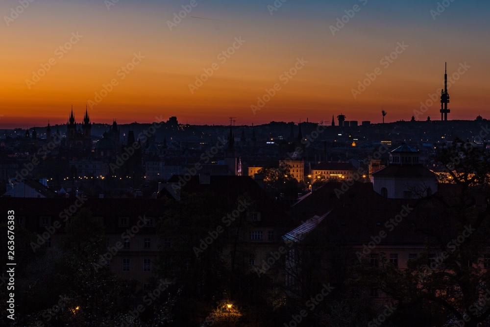 Prague, capital city of the Czech Republic, at dawn, silhouette of Zizkov tower on horizon, red, yellow, blue and orange sky, urban landscape with houses in shadow, panoramic view