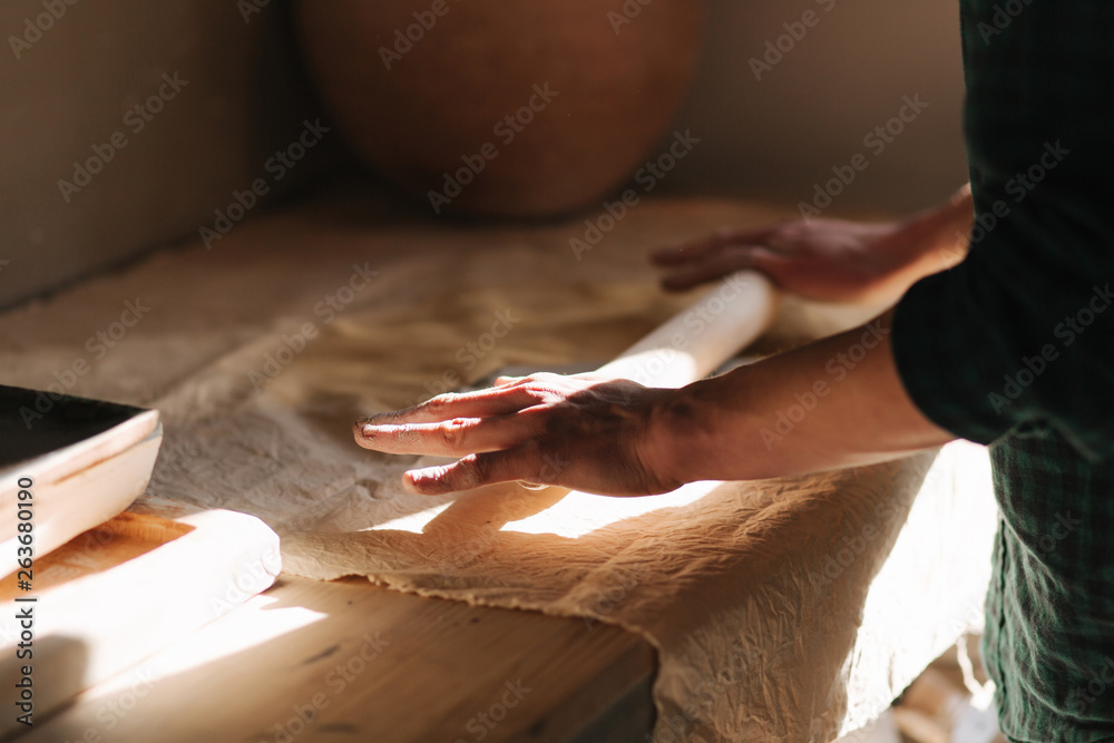 Obraz premium Male potter use rollong pin for clay. Man in workshop