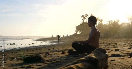 A handsome man deep breathing and meditating at sunset on a picturesque California beach with palm trees in silhouette. photo