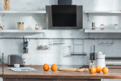 modern kitchen with juicer, glass and tasty organic oranges on wooden table
