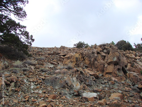 The landscape of the rocky surface of the top of the mountain ridge covered with poor vegetation on the background of the cloudy sky.