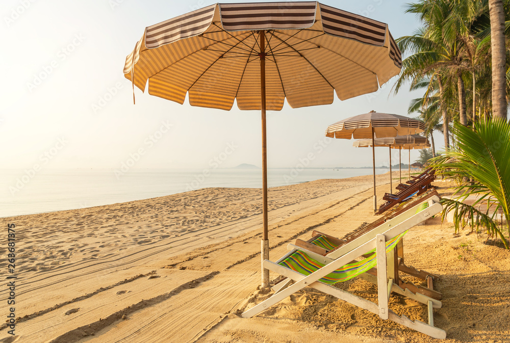 Row of empty wooden beach chairs with parasols on tropical sandy beach in the morning  relax leisure concept