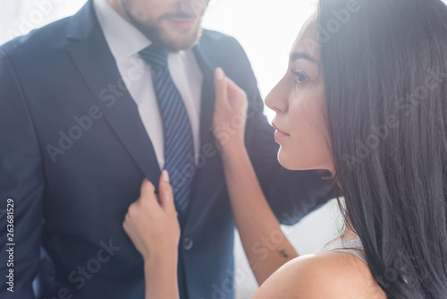 Fototapeta Naklejka Na Ścianę i Meble -  attractive brunette girl touching formal wear of bearded man