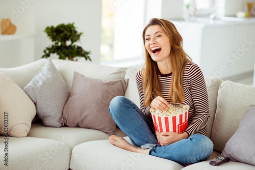 Close up photo beautiful she her model lady hands big container corns arms laughing loud comic serial fast food wear jeans denim striped pullover clothes sit comfort divan house living room indoors