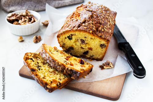 Appetizing beautiful bread or loaf cake with nuts, dried fruits cut into pieces on a wooden cutting board. Copy space.