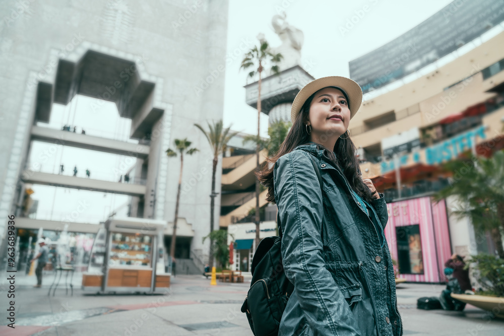 Traveler backpacker asian woman travel in Hollywood Boulevard sightseeing. Happy young female in straw hat spending spring holiday trip at amazing landmark. girl enjoy journey in modern city urban