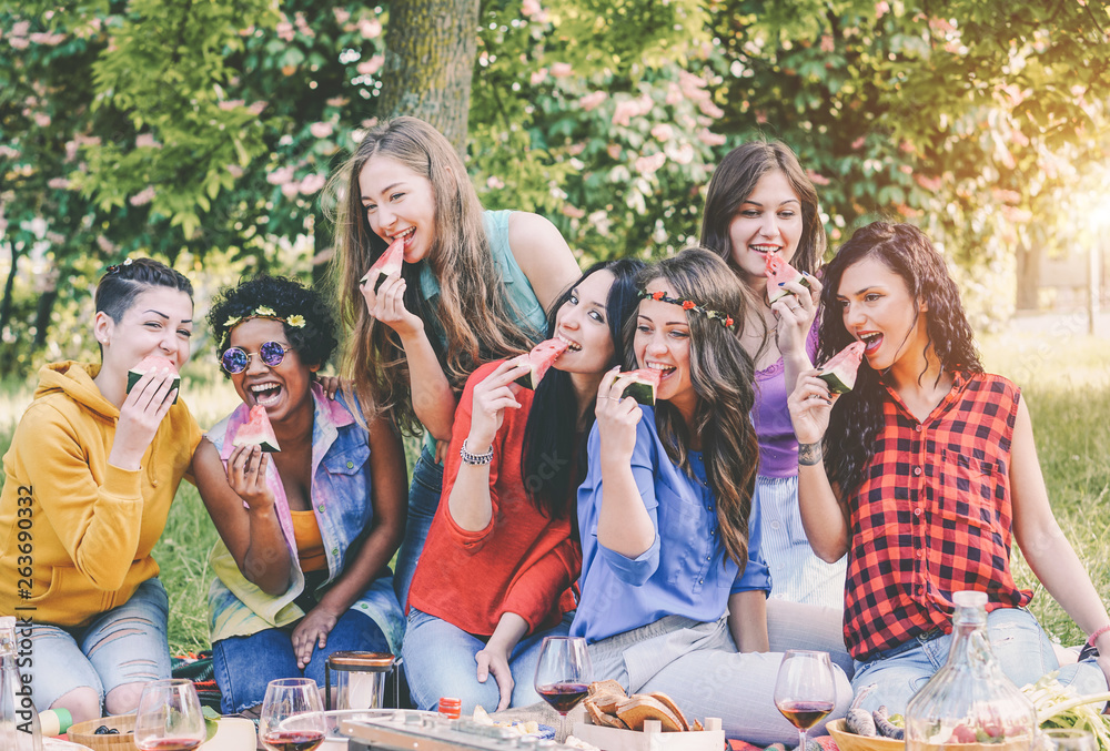 Happy girls eating watermelon at picnic dinner in the garden - Young women having fun enjoying lunch together in the backyard - Friendship, food, weekend activities and youth lifestyle concept