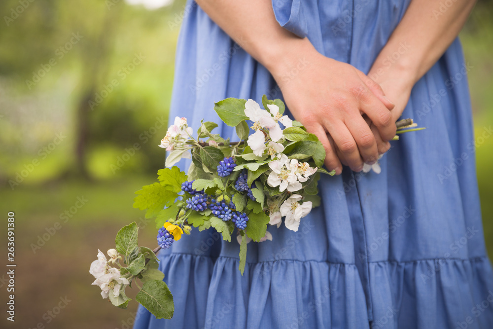 A bouquet of spring flowers in the hands of a girl on a background of blue dress. Blooming apple tree in spring park.